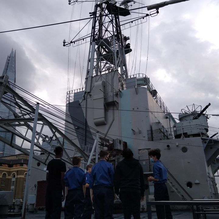 An image showing a group of cadets standing on the boat deck of HMS Belfast with the Shard in the background