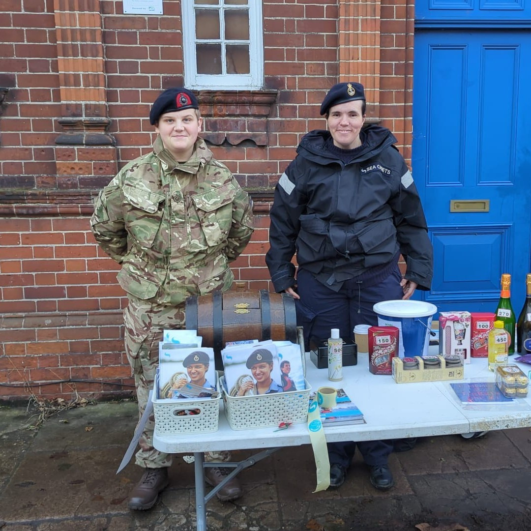 Royal Marine Cadet York and Petty Officer Rosenstiel stood behind the tombola and recruiting stall at the Mill Road Winter Fair.